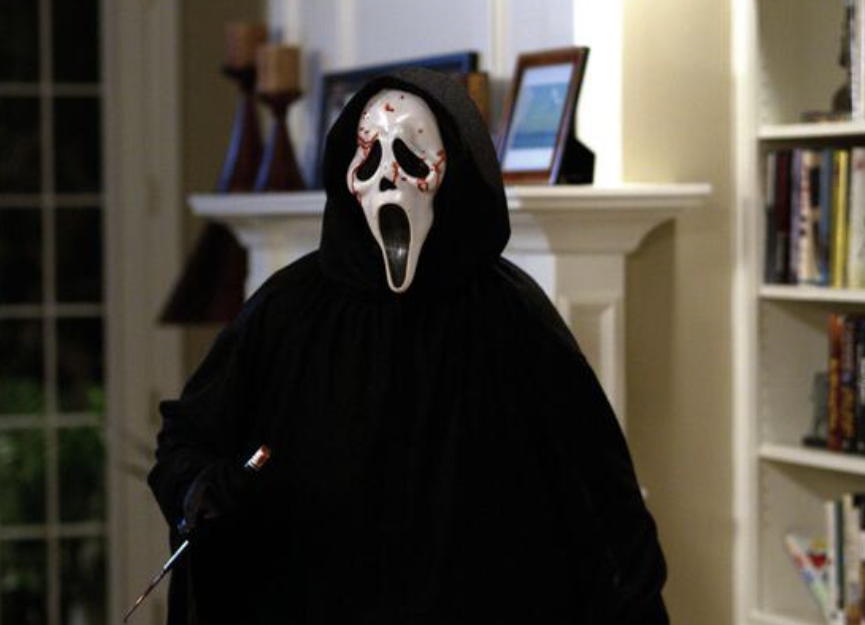 Una persona con una capa negra y una máscara facial fantasma sosteniendo un cuchillo ensangrentado. spooky season